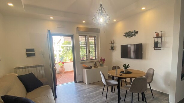 A modern living room with a sofa, dining area with chairs, a TV mounted on the wall, and a ceiling light fixture. - Entire apartment with terrace, free parking, free wi-fi (Vico Equense)