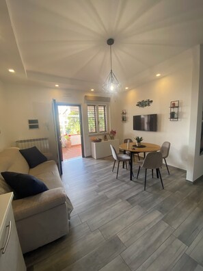 A modern living room with a sofa, dining area with chairs, a TV mounted on the wall, and a ceiling light fixture. - Entire apartment with a terrace, free parking, and free Wi-Fi (Vico Equense)