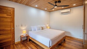 Une chambre avec un plafond en bois, un lit avec une literie blanche, une table de chevet avec une lampe et un appareil de climatisation fixé au mur.