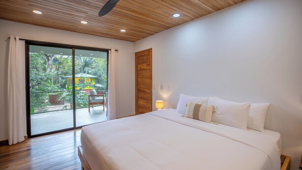 Une chambre dotée d’un grand lit, d’un ventilateur de plafond et offrant une vue sur un balcon aménagé avec du mobilier d’extérieur.