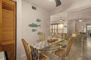 Uma área de refeições com mesa de vidro, cadeiras de vime e parede decorada com adesivos de peixes.