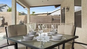 Une terrasse extérieure avec une table en verre, mise pour le repas, entourée de chaises.