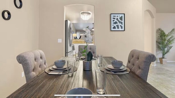 Un coin repas avec une table en bois dressée pour quatre personnes, deux chaises, un lustre et une œuvre d’art abstraite encadrée accrochée au mur.