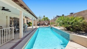 Une piscine rectangulaire dont le bord est revêtu de carrelage, entourée d’un patio couvert aménagé avec des chaises et des tables.
