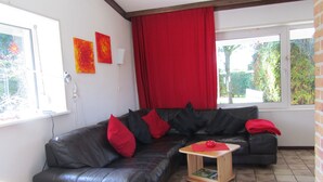 A living room with a dark leather sofa, red cushions, a small wooden table with a red object, and a red curtain. - Vacation home Holland, 2 -4 pers., sea, dog, gas fireplace, wifi  (Sint Maartensvlotbrug)