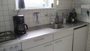 A kitchen with a gas stove, a coffee maker, a sink, and various kitchen utensils. - Vacation home Holland, 2 -4 pers., sea, dog, gas fireplace, wifi  (Sint Maartensvlotbrug)