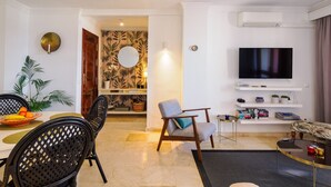 Een moderne woonkamer met een flatscreen televisie, een eethoek met tafel en stoelen, en een gang met een spiegel en tropische behang.