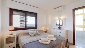 Habitación de hotel con cama, mesita de noche con lámpara, cómoda, espejo y ventana con persianas.