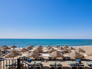 A beach with rows of sun loungers and thatched umbrellas.