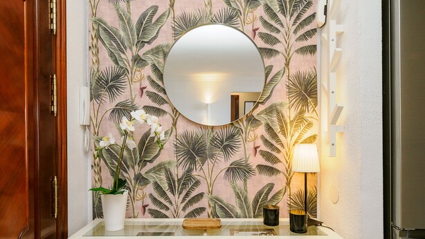 Un baño con tocador blanco, espejo redondo, planta en maceta y lámpara de pared.