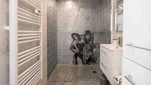Casa de banho moderna com chuveiro, paredes em azulejo, toucador branco e chão em mosaico.