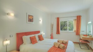 A hotel room with a bed, bedside table, lamp, and a window with curtains. - Monte Laranja Apt in Lagos (Lagos)