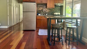 A kitchen with wooden cabinets, a stainless steel refrigerator, a marble backsplash, and a window with a view.