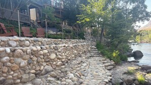 A stone retaining wall with a river on one side and a building with outdoor seating in the background.