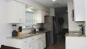 A kitchen with white cabinets, a granite countertop, a refrigerator, and a dishwasher. - Orlando 3 Bedroom Close to Disney (Orlando)
