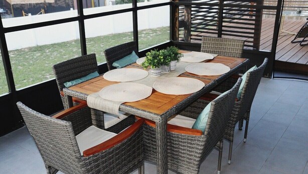 A covered patio with a wooden table and wicker chairs, surrounded by large windows. - Orlando 3 Bedroom Close to Disney (Orlando)
