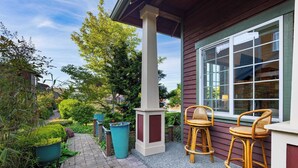 Un espace patio comprenant deux tabourets de bar en osier, une plante en pot et une poubelle.
