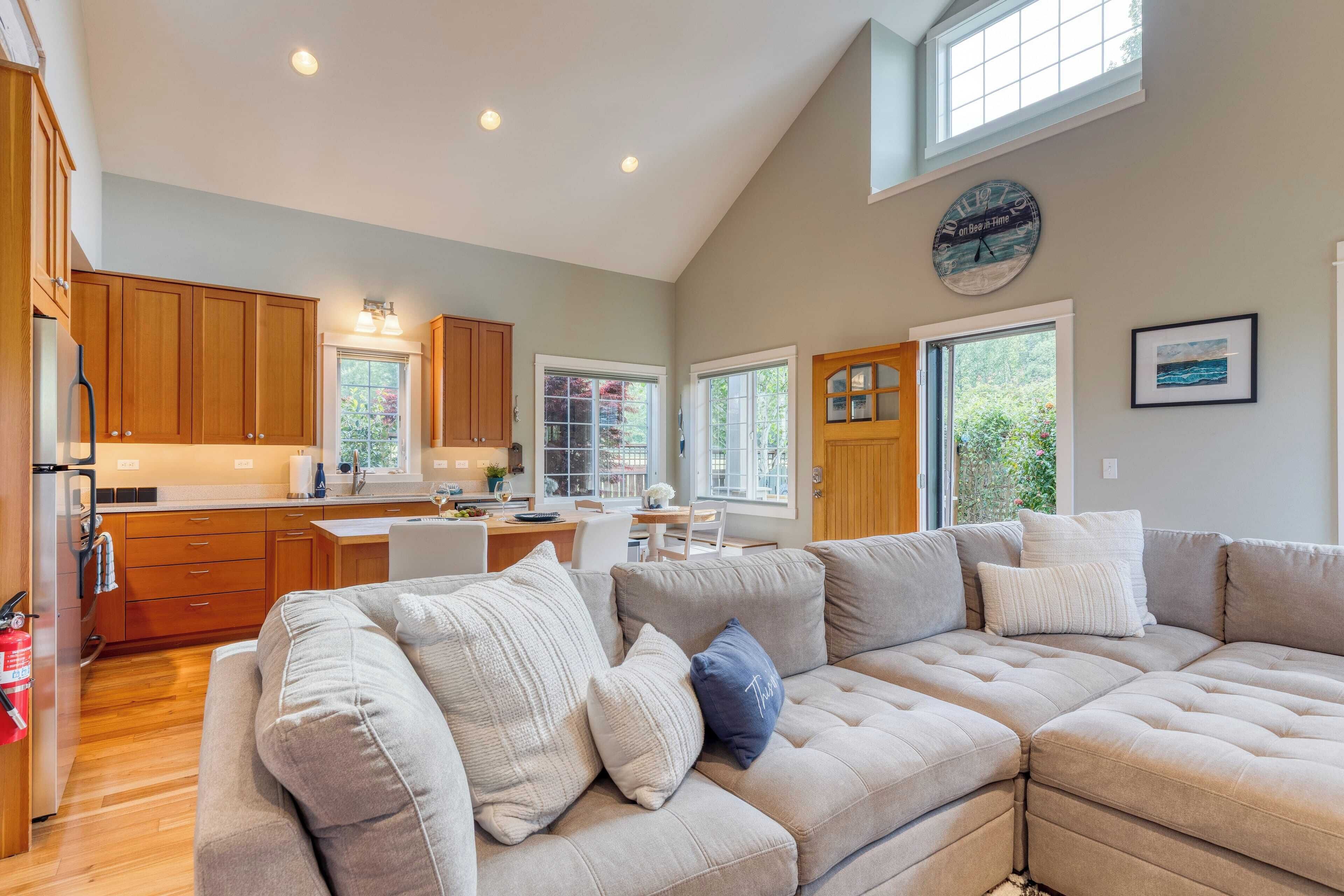 A spacious living area with a large sectional sofa, wooden cabinets, and a kitchen in the background.