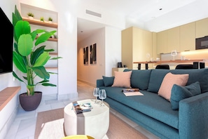 A modern living room with a sofa, a coffee table, a potted plant, and a kitchen in the background.