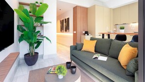 Ein modernes Wohnzimmer mit einem großen Flachbildfernseher, einem grünen Sofa mit gelben Kissen, einem Couchtisch mit einer Pflanze und einem Blumentopf.