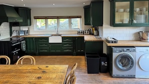 Una cucina moderna con mobili verdi, un tavolo di legno, forno integrato, microonde, lavello e lavatrice.