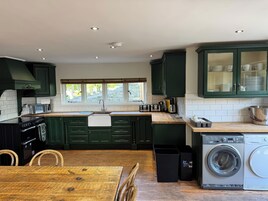 Una cocina moderna con armarios verdes, una mesa de madera, horno empotrado, microondas, pileta y lavadora.