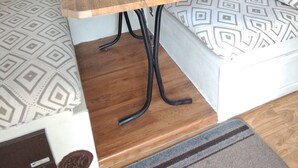 A compact RV interior with a wooden table, patterned sofa, and a small window with curtains. - Cute RV in the  forested mountains at Cedar Ridge,  Sonora for your vacation. (Sonora)