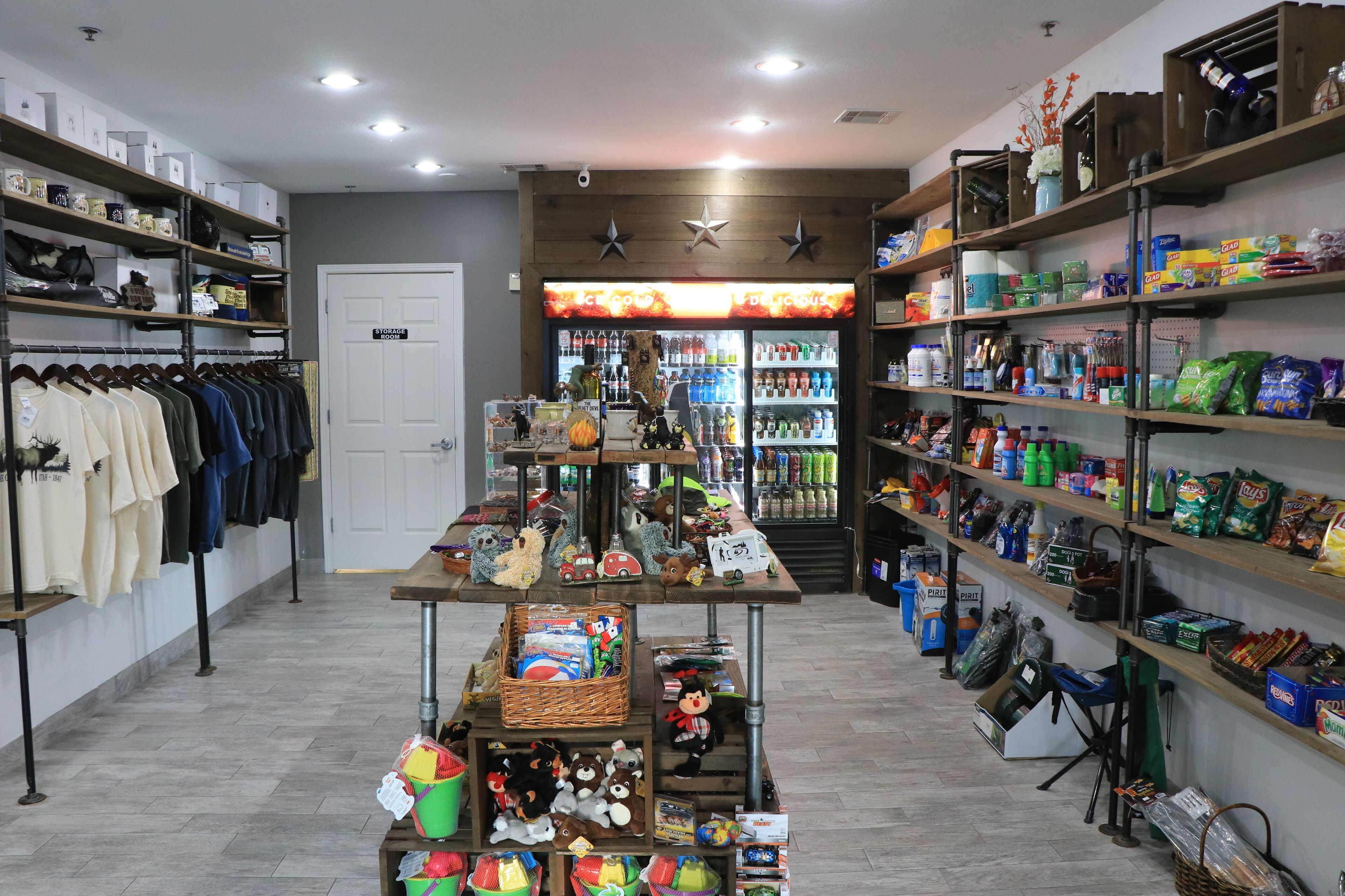 Una tienda con estantes llenos de diversos productos, un perchero y una mesa expositora con juguetes y juegos.