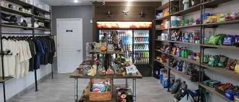 Una tienda con estantes llenos de diversos productos, un perchero y una mesa expositora con juguetes y juegos.