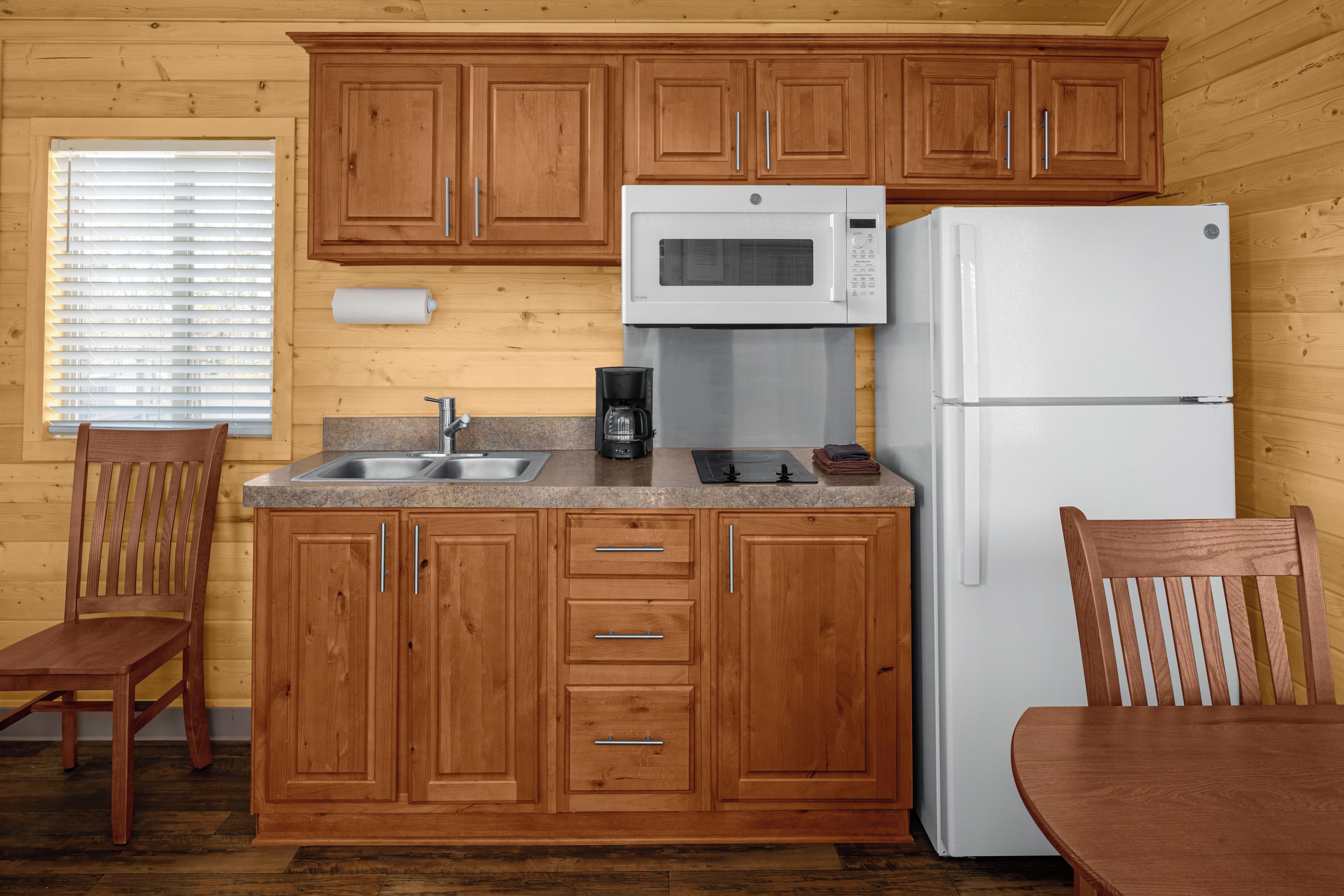 Una cucina compatta con mobili in legno, un frigorifero bianco, un forno a microonde e una macchina per il caffè.