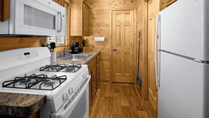 Una cocina compacta con estufa a gas, microondas y refrigerador, armarios de madera y un lavamanos.