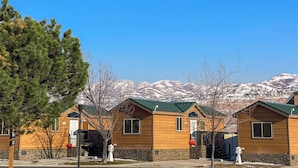 A row of wooden cabins with stone foundations, set against a backdrop of snow-capped mountains and clear blue sky. - Sun Outdoors Salt Lake City (North Salt Lake)