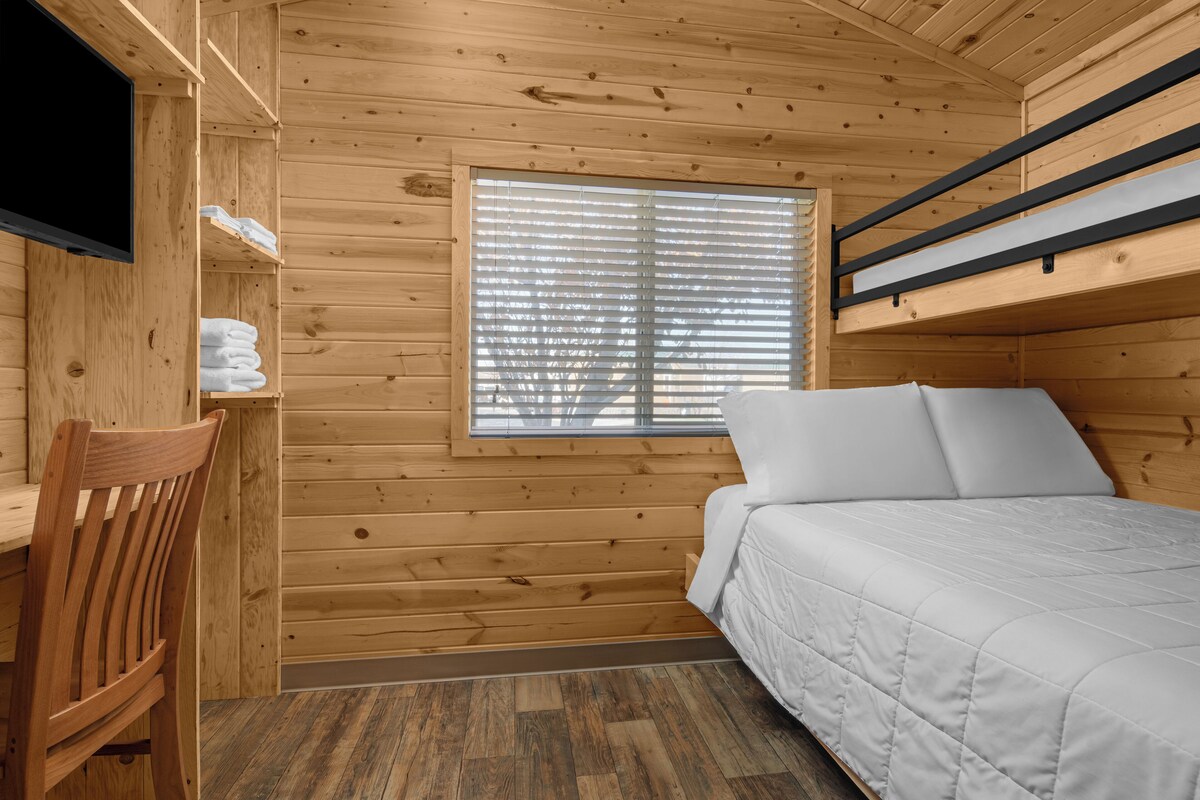 Una habitación tipo cabaña de madera con una cama litera, un escritorio y una silla.