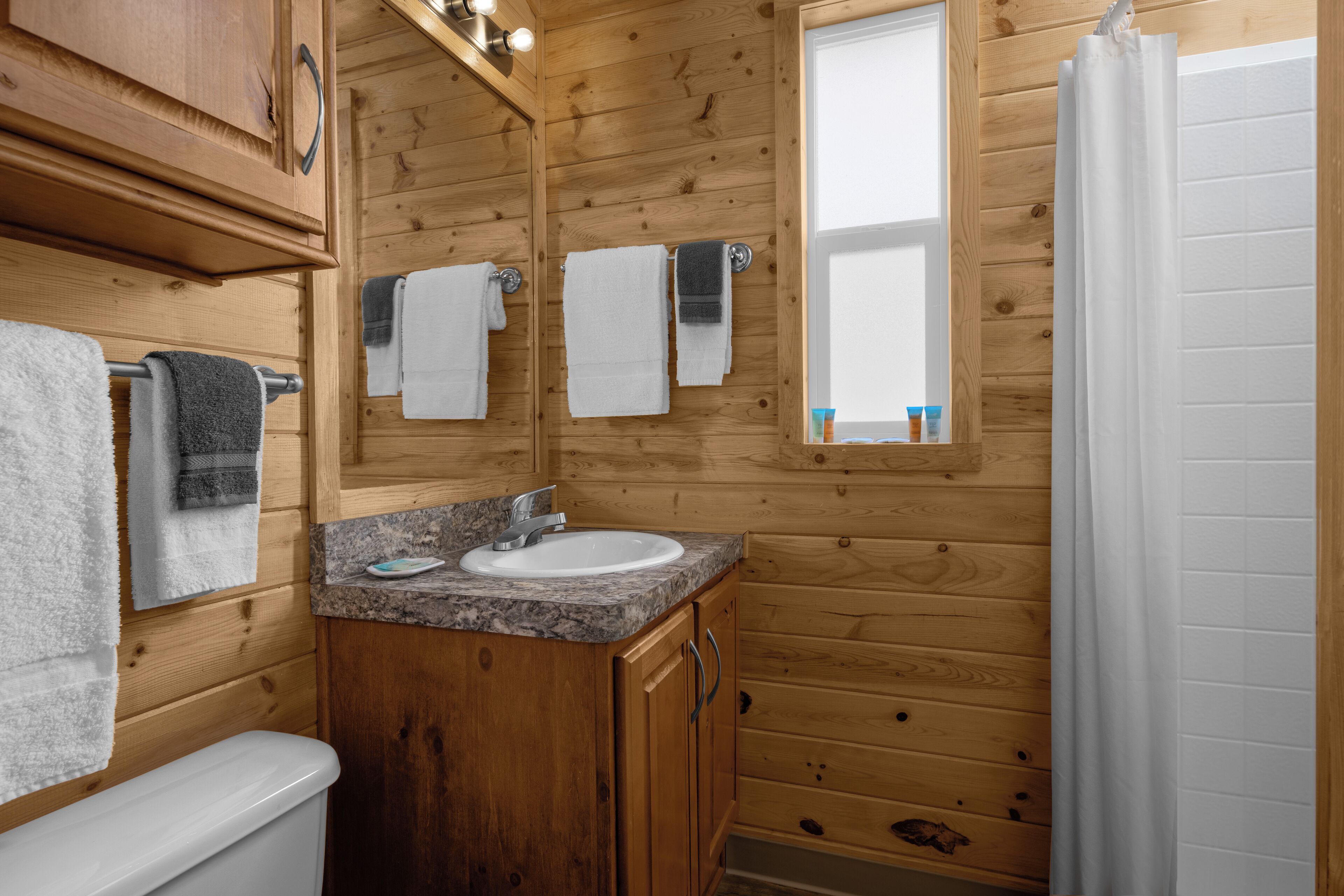 Un baño de cabaña de madera con lavamanos, espejo y toallero.