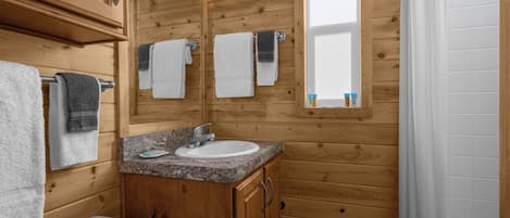 Un baño de cabaña de madera con lavamanos, espejo y toallero.