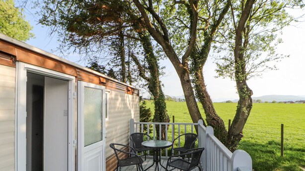 Een terras met een tafel, stoelen, een deur en uitzicht op een groen veld en bomen.