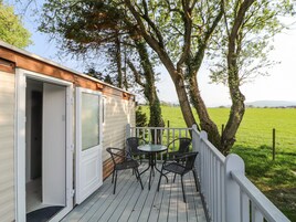 A deck with a table and chairs, a door, and a view of a green field and trees.