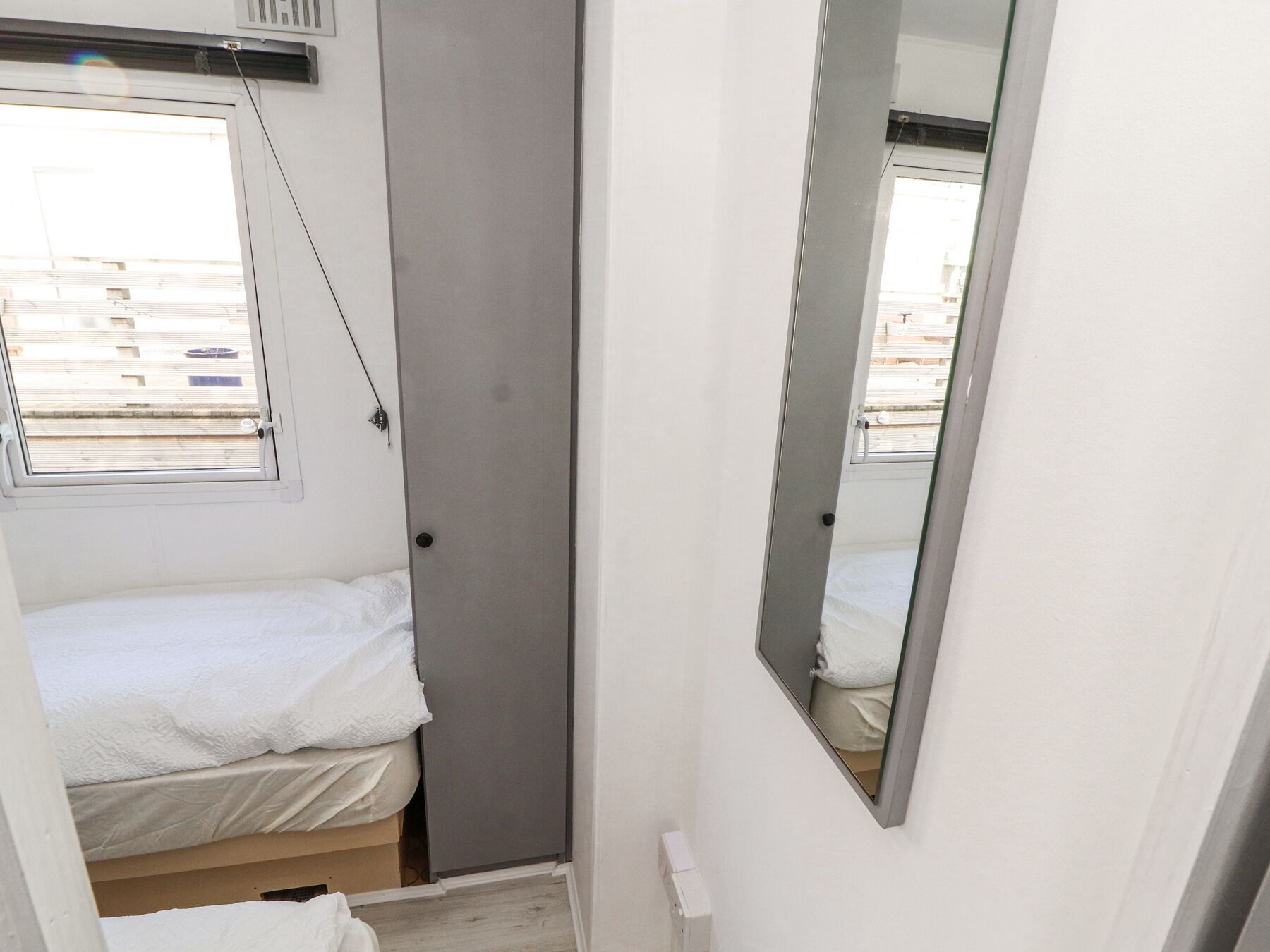 A small, narrow room with a single bed, a door, and a window.