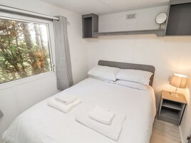A neatly made bed with white linens and towels, a bedside table with a lamp, and a window with a view of trees.