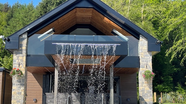 A modern building with a pool, stone pillars, and a wooden roof. - Forest Lodge (Pontyclun)