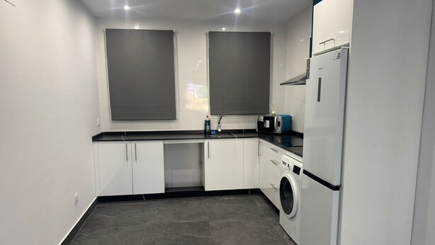 A compact kitchen with white cabinets, a washing machine, a microwave, and a refrigerator. - Fast Latin Home (Seville)