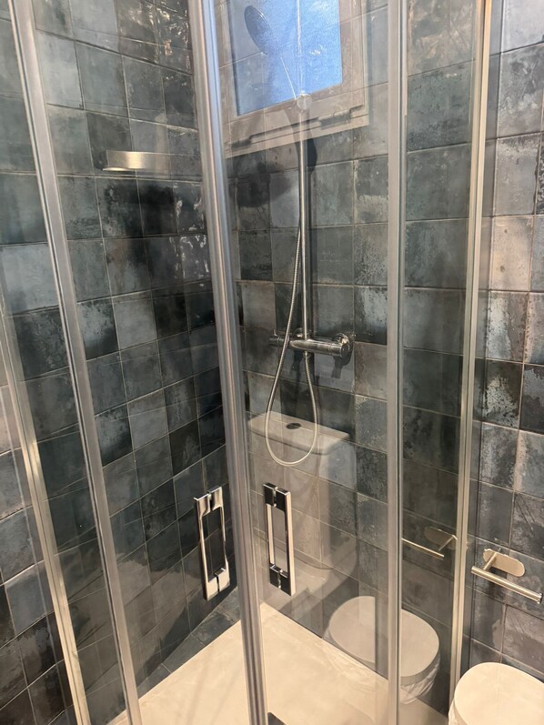 A glass-enclosed shower stall with a handheld showerhead, a wall-mounted faucet, and a toilet. - Fast Latin Home (Seville)
