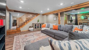 A modern living room with a wooden staircase, grey sofa, and a patterned rug. - Private Pickleball Court, Sauna, Hot Tub, Heart of Branson, Sleeps 13! (Branson)