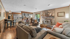A spacious living area with a fireplace, wooden flooring, and a kitchen in the background. - Private Pickleball Court, Sauna, Hot Tub, Heart of Branson, Sleeps 13! (Branson)