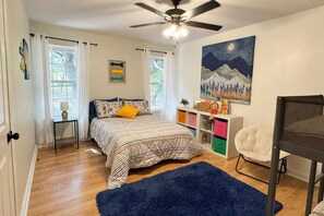 Ein Schlafzimmer mit einem Bett, einem Deckenventilator, einem Gemälde von Nachthimmel, einem Bücherregal und einem Sessel.