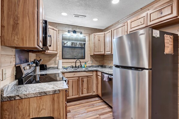 A modern kitchen with wooden cabinets, stainless steel appliances, granite countertops, and a window with blinds.