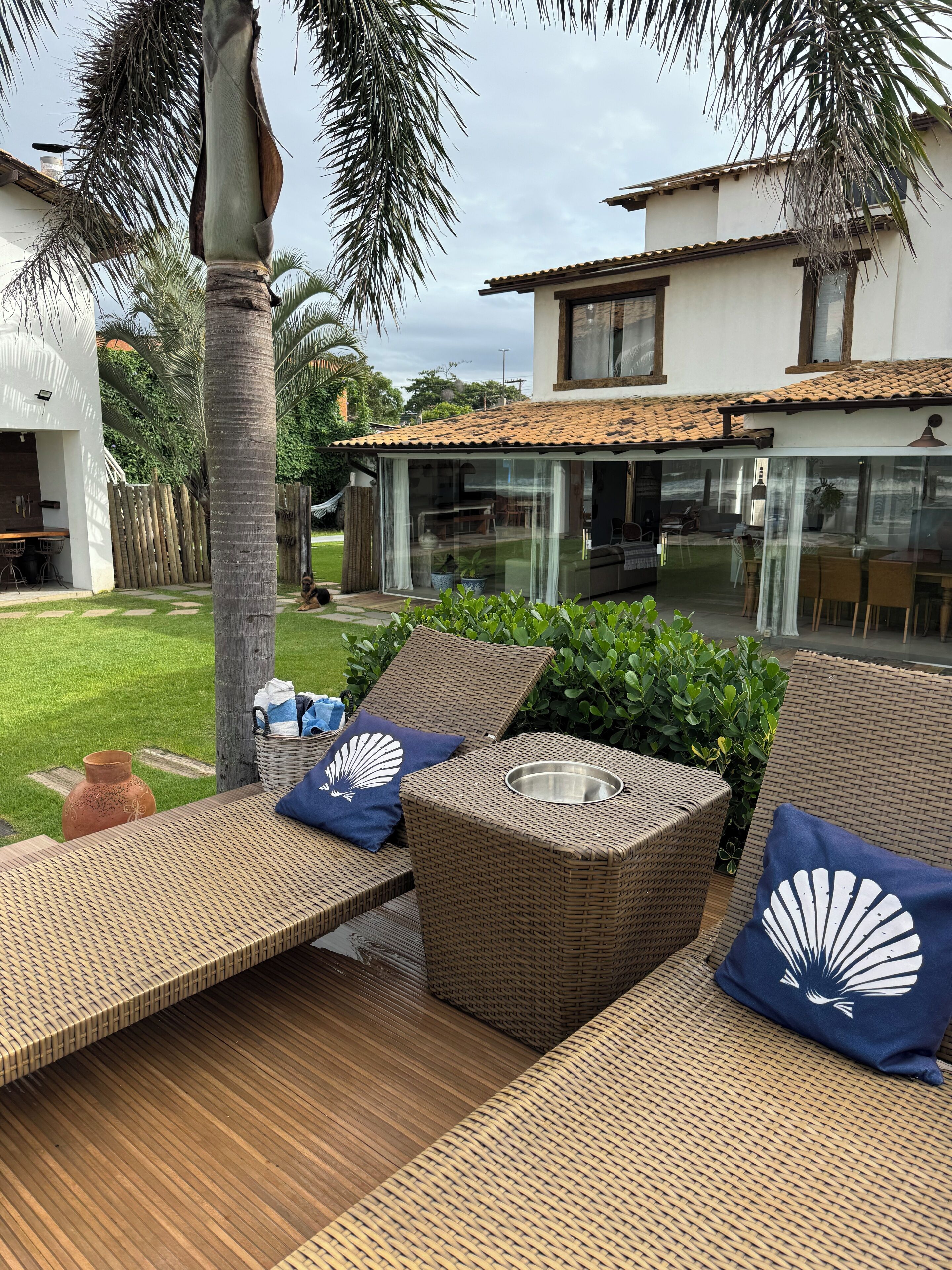 Uma área de pátio com móveis de vime, um compartimento envidraçado e vista para a casa.