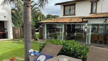 Uma área de pátio com móveis de vime, um compartimento envidraçado e vista para a casa.