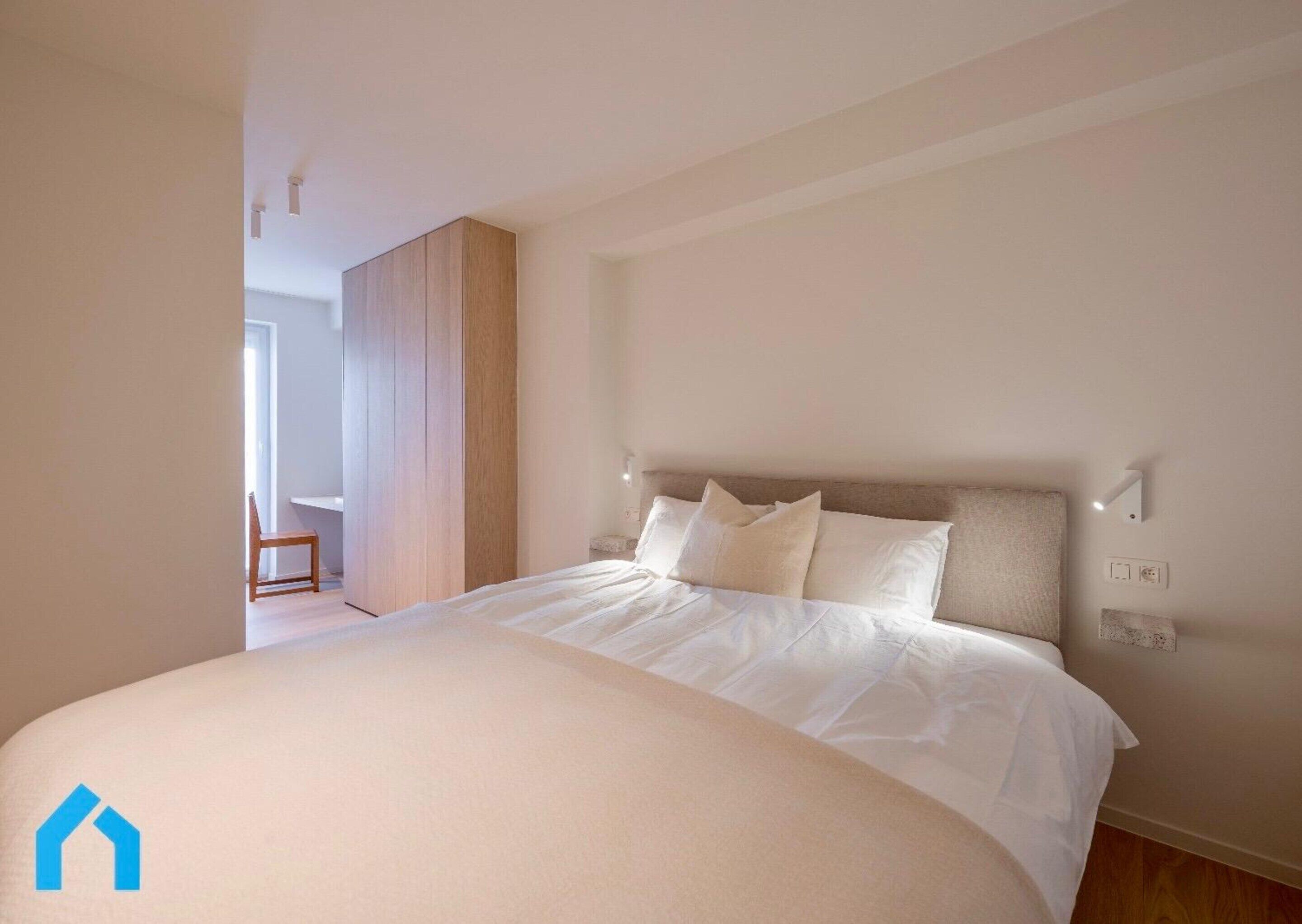 A bedroom with a large bed, a wooden wardrobe, and a chair.