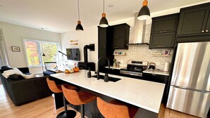 Een moderne keuken met een centraal eiland, barstoelen, roestvrijstalen apparatuur en donkere keukenkastjes.